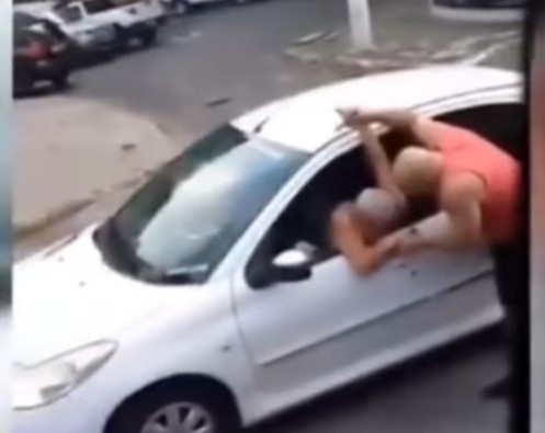 Homem quebra o braço de idoso durante discussão no trânsito. Ele segura a mão do idoso, que está sentado dentro do seu carro.