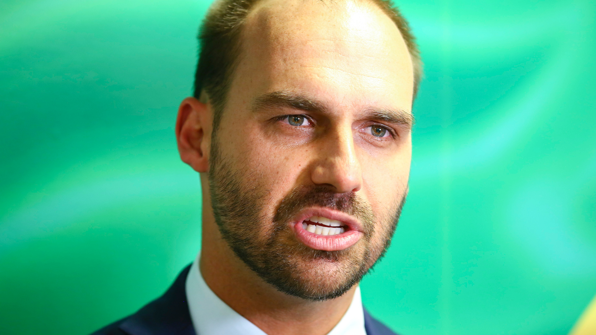 Eduardo Bolsonaro faz piada com tortura sofrida por Míriam Leitão na ditadura. Foto de Eduardo Bolsonaro falando. Ele usa um terno azul e barba.