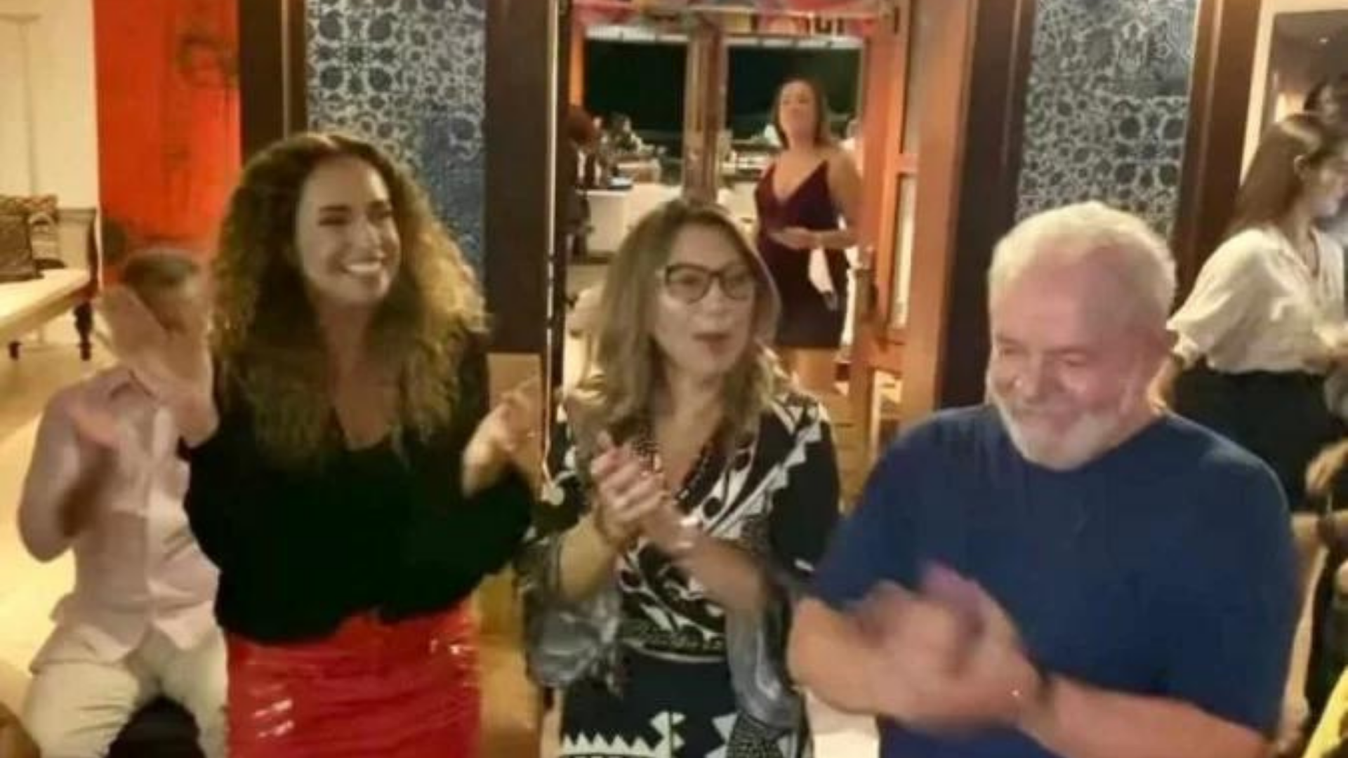 Lula dança ao lado de Daniela Mercury. O ex-presidente aparece em foto com uma camisa azul, ao lado de Daniela Mercury e Janja, que estão sorrindo e dançando no terraço da casa.