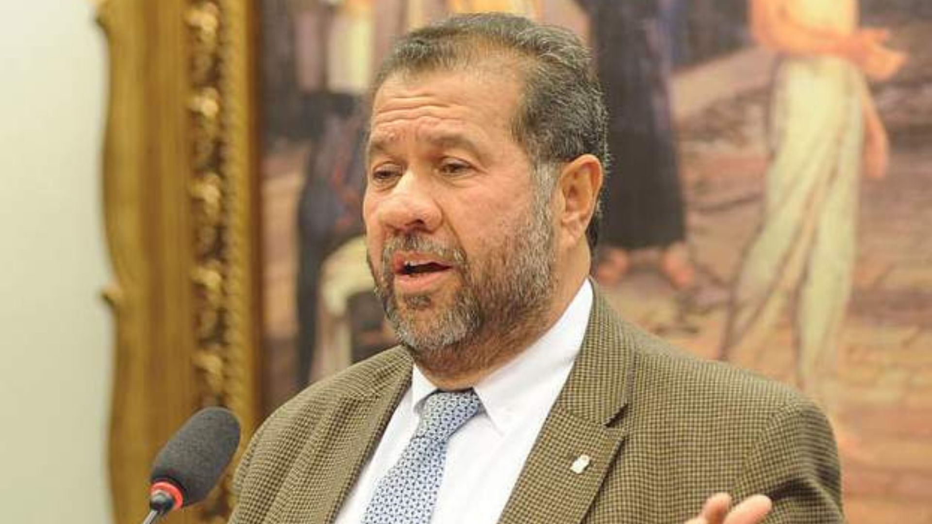 Foto de Carlos Lupi usando terno marrom, cabelo grisalho e barba.