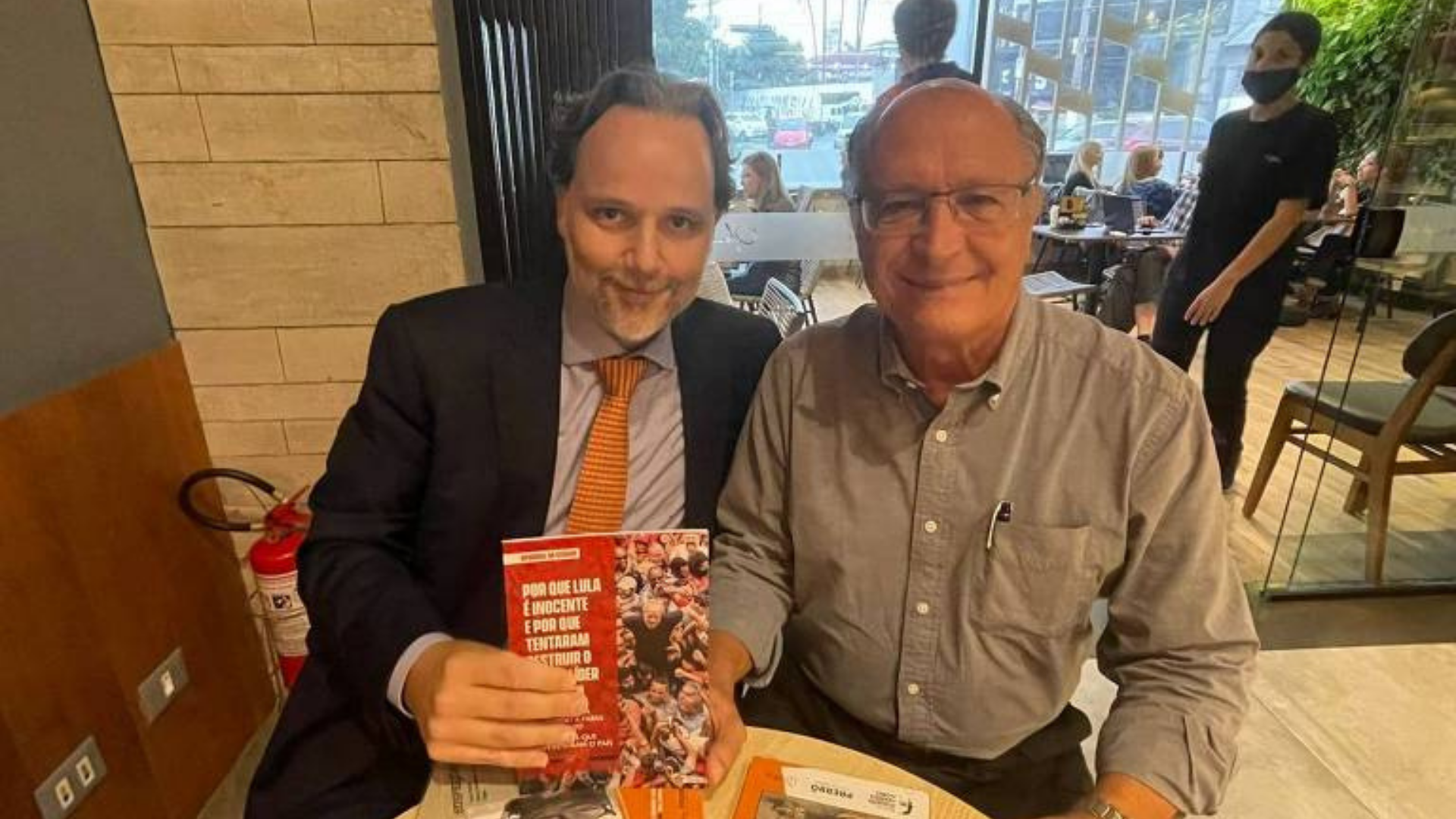 Alckmin posta foto segurando livro sobre Lula. Foto de Alckmin sorrindo em uma mesa ao lado de um advogado do grupo Prerrogativas, que segur ao livor.