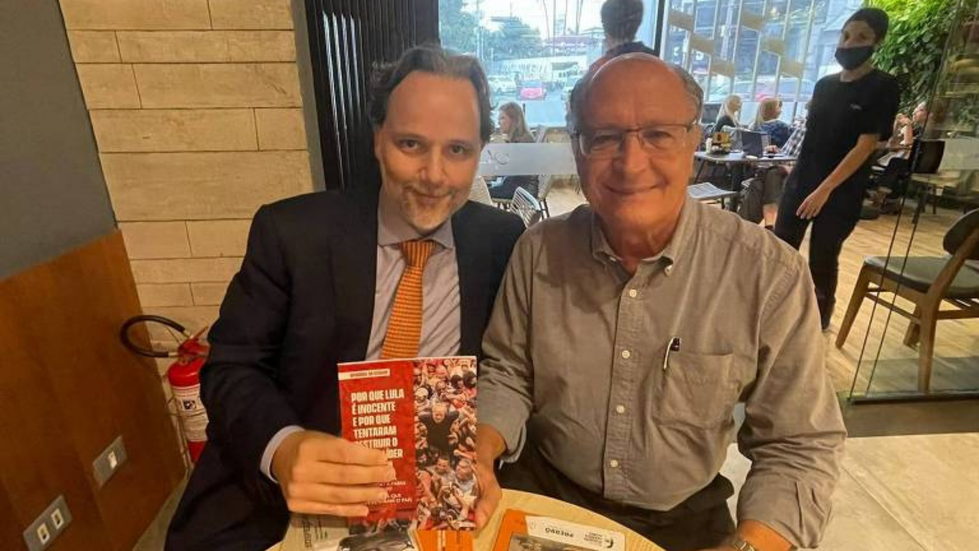 Alckmin posta foto segurando livro sobre Lula. Foto de Alckmin sorrindo em uma mesa ao lado de um advogado do grupo Prerrogativas, que segur ao livor. 