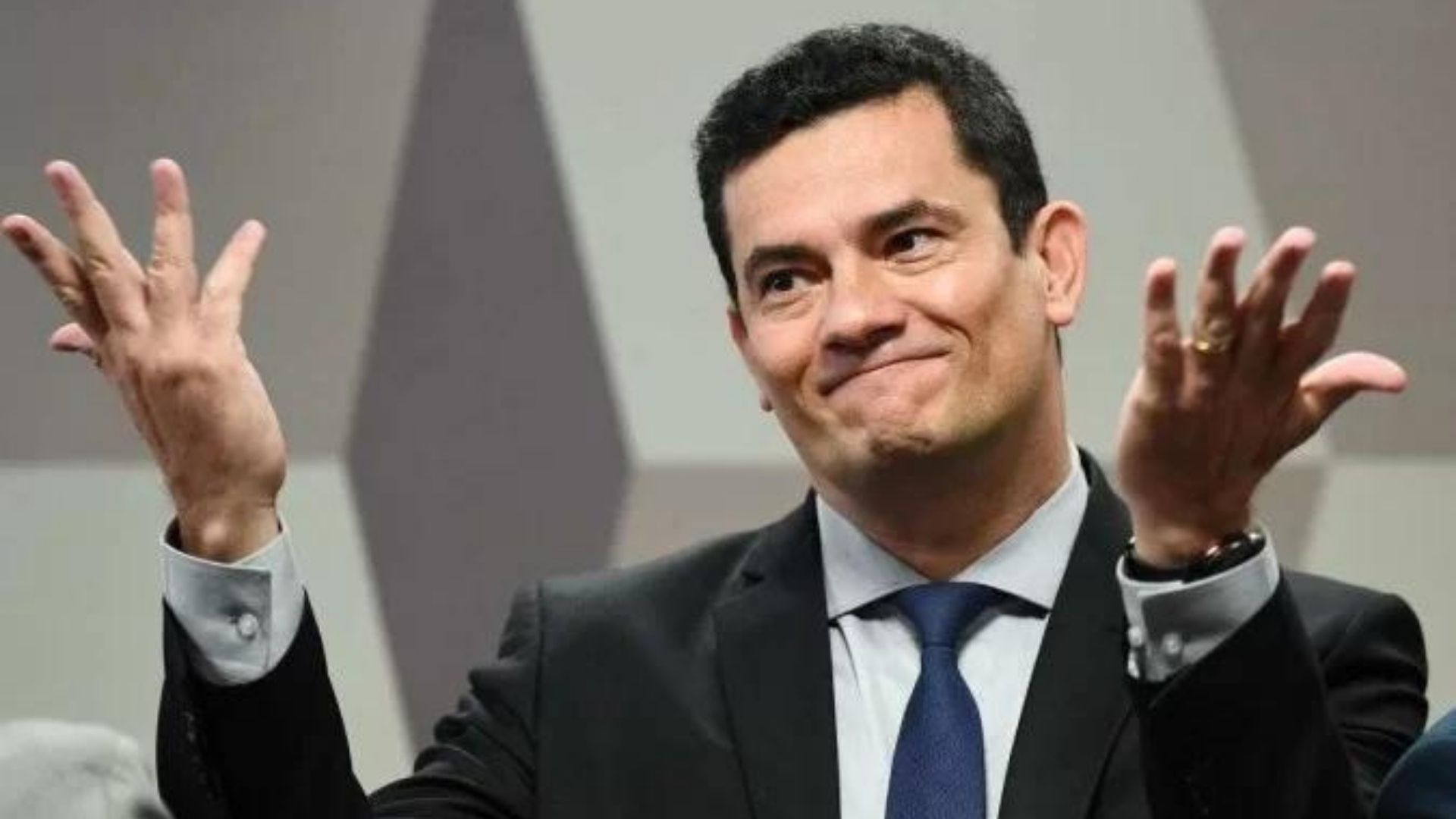 Foto d eSergio Moro com os braços na altura dos ombros. Ele está sentado e faz sinal de desentendimento.