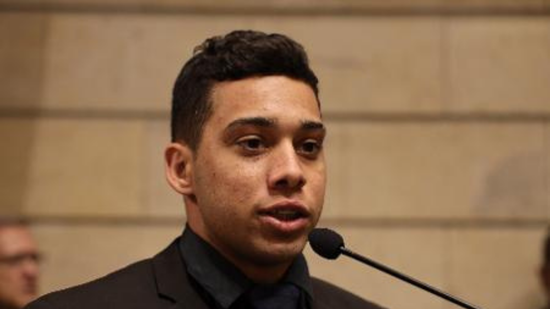 Gabriel Monteiro usa terno preto e fala ao microfone no plenário.
