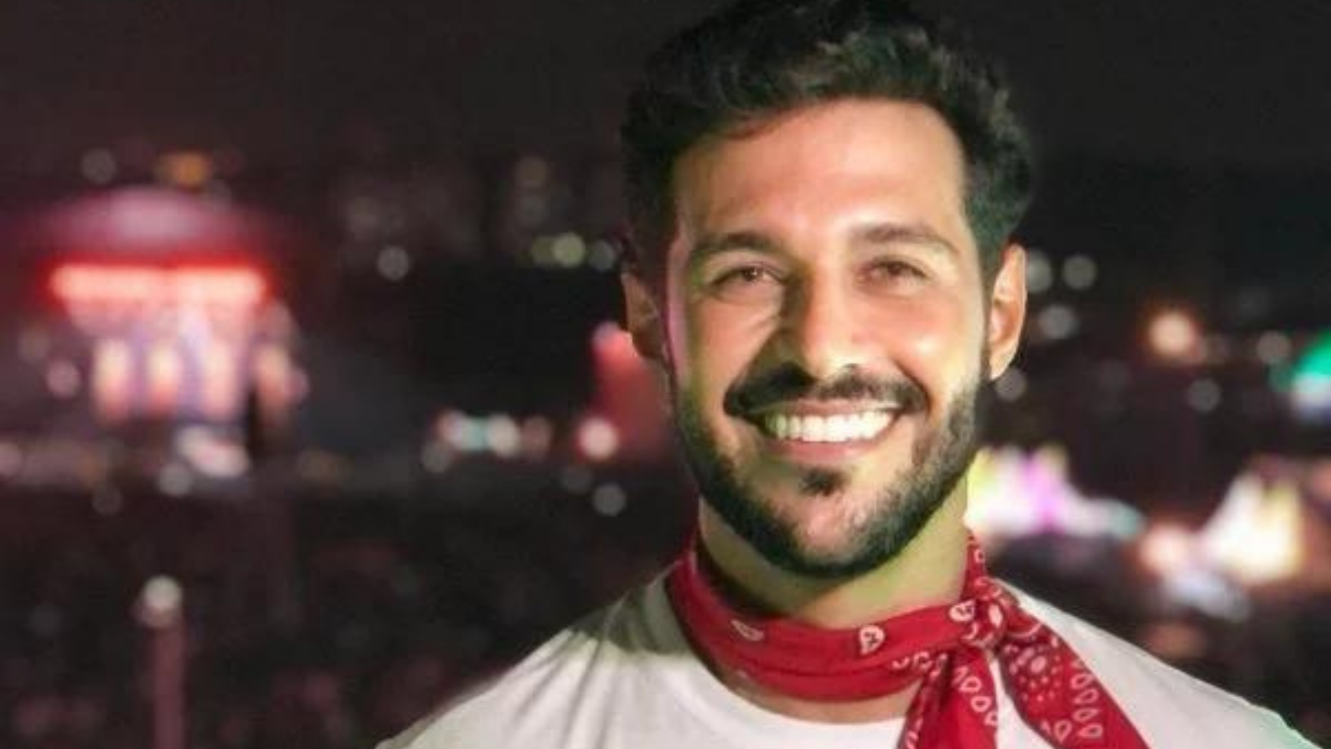 Nova atualização do estado clínico do ex-BBB Rodrigo Mussi é divulgada. Foto de Rodrigo Mussi sorrindo com um cachecol vermelho.