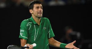 Foto de Djokovic com camisa verde, braços na altura dos cotovelos e expressão de desentendido.