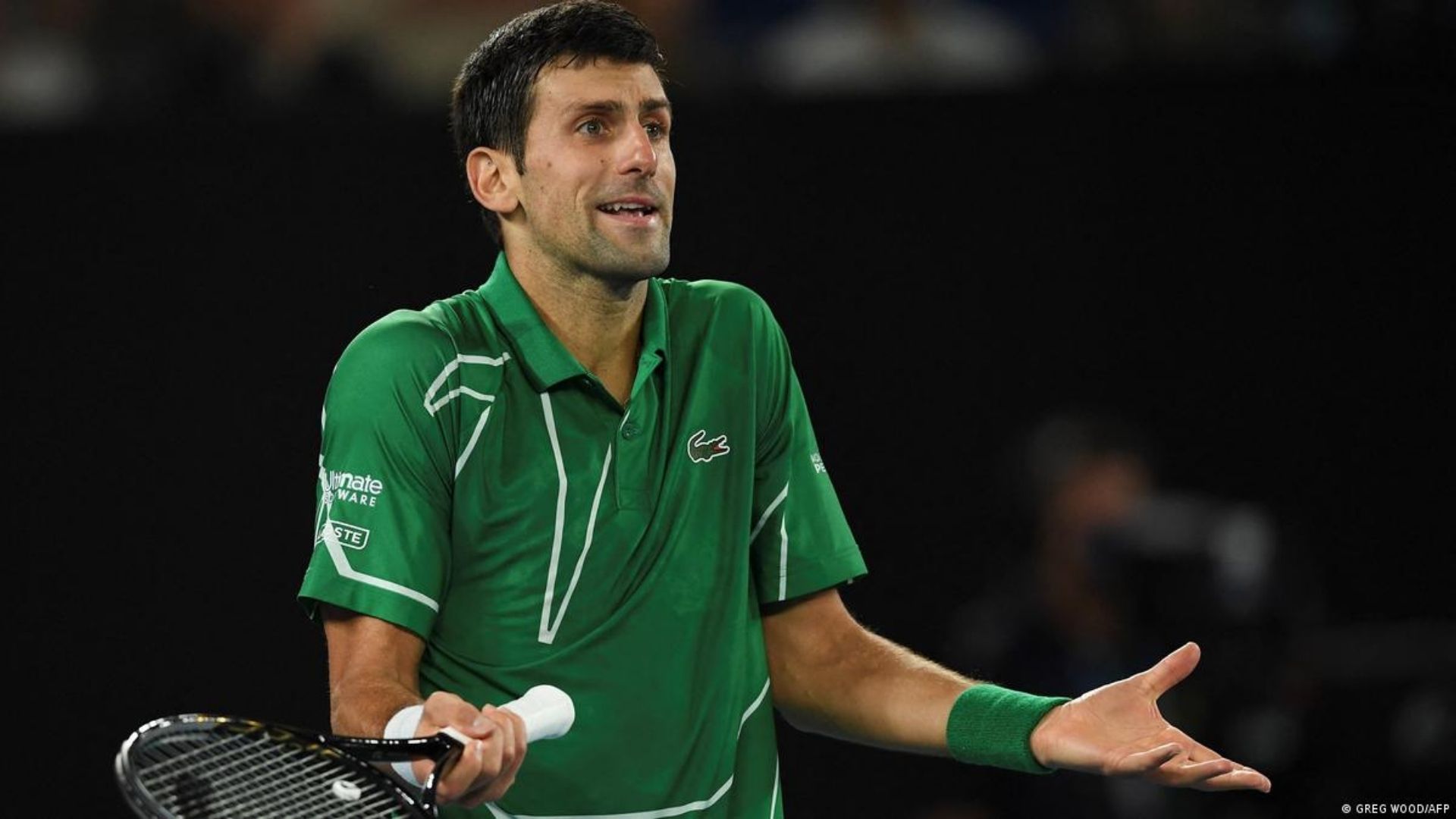 Foto de Djokovic com camisa verde, braços na altura dos cotovelos e expressão de desentendido.
