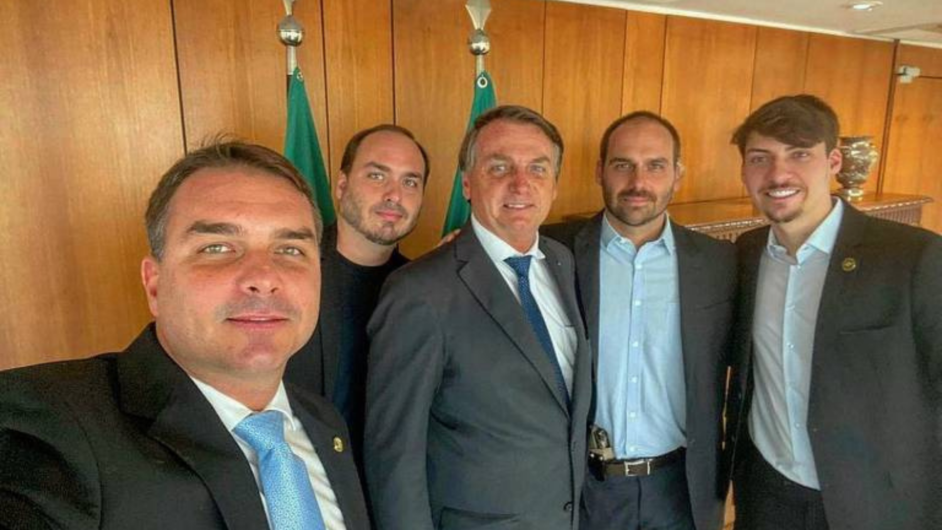 Imagem do presidente Bolsonaro junto com os filhos. Eles estão um ao lado do outro e sorriem para uma selfie.