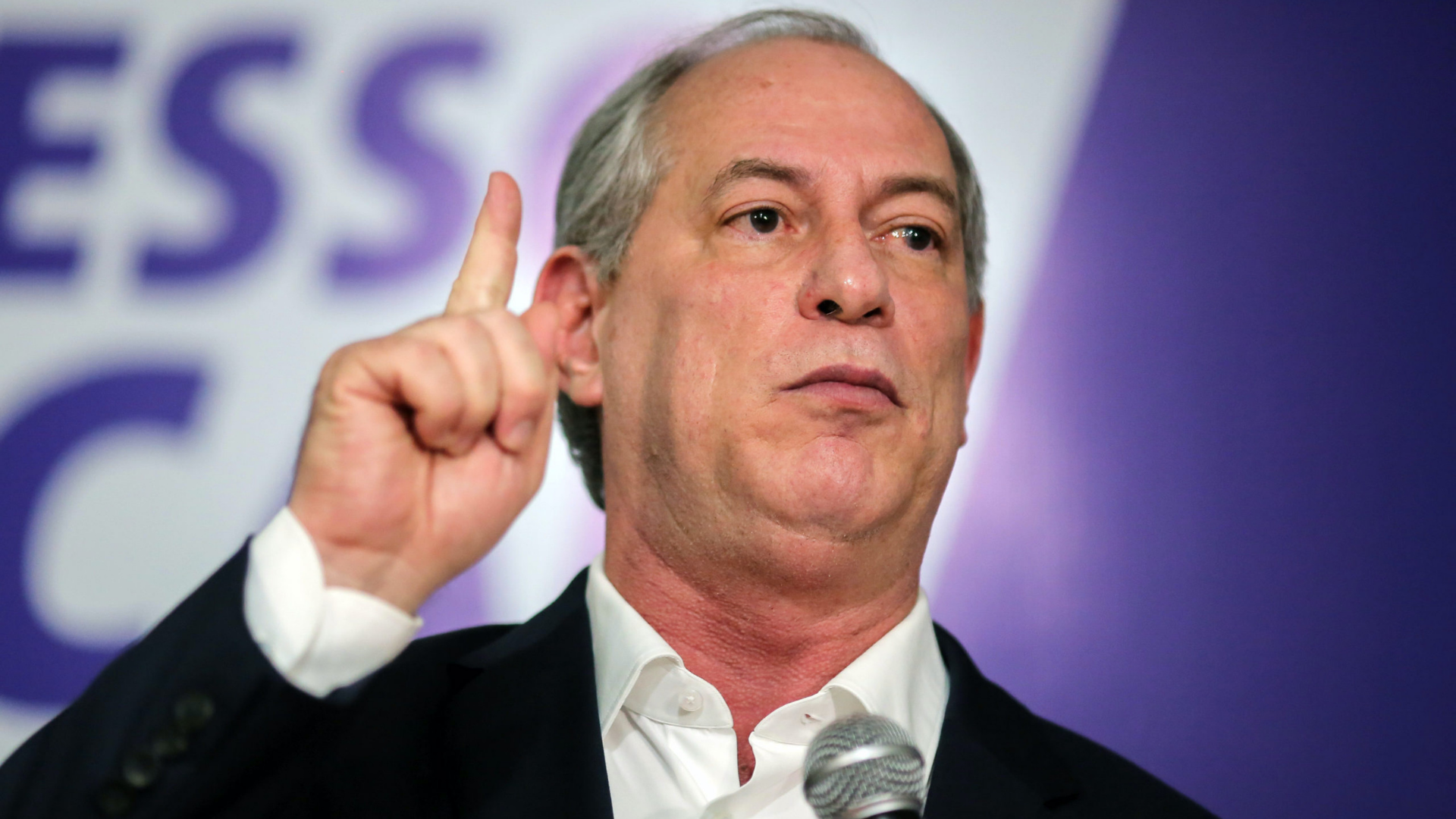 Foto de Ciro Gomes com boca aberta e dedo indicador apontado para cima.