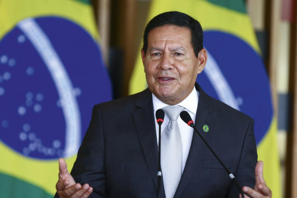 Foto de Hamilton Mourão em um púlpito falando ao microfone. Ao lado, há uma bandeira do Brasil.