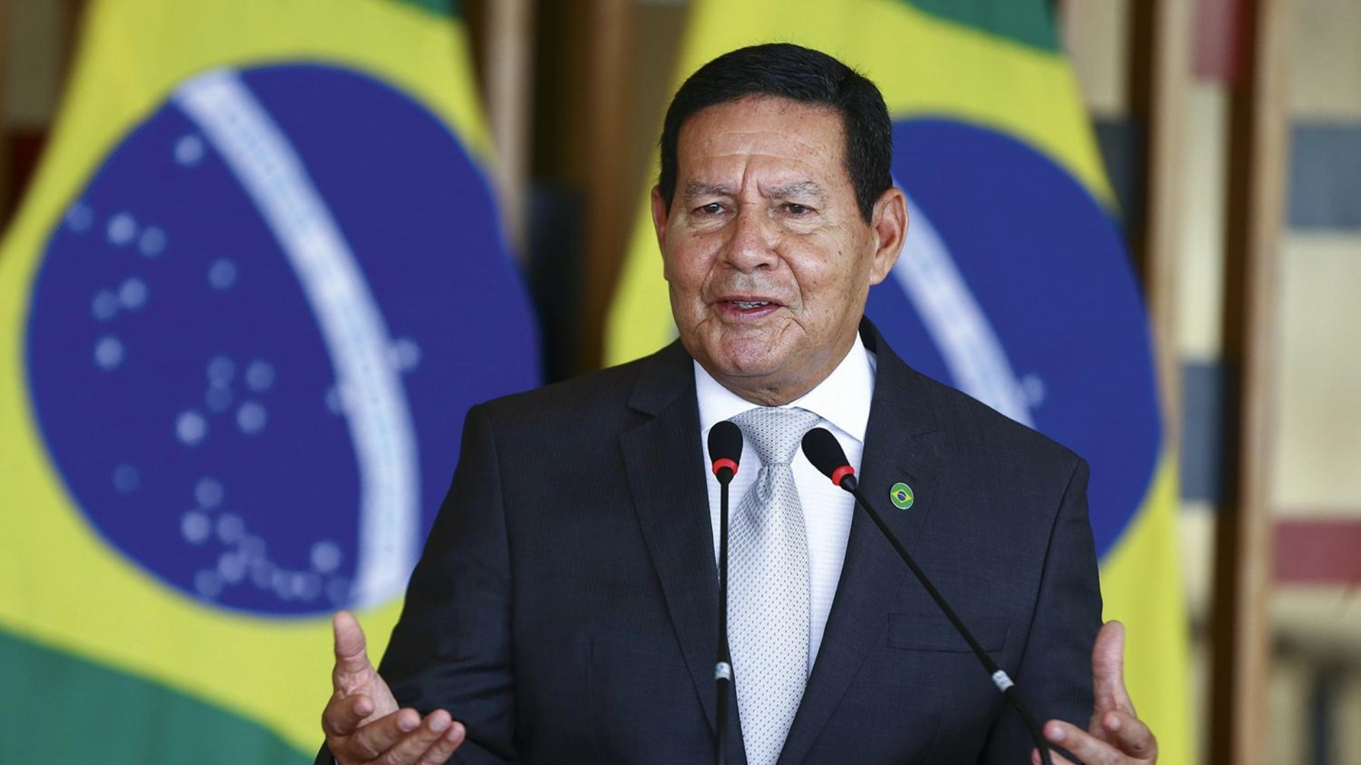 Foto de Hamilton Mourão em um púlpito falando ao microfone. Ao lado, há uma bandeira do Brasil.