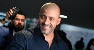 Daniel Silveira sorri para foto. Ele usa uma camisa social azul marinho.