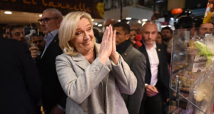 Marine Le Pen sorri para alguém e tem as mãos no formato de oração, demonstrando esperança.