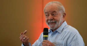 Foto do ex-presidente Lula falando ao microfone com um sorriso no rosto.