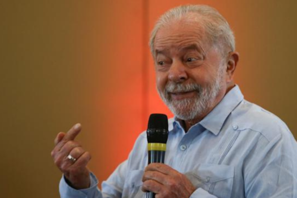 Foto do ex-presidente Lula falando ao microfone com um sorriso no rosto.