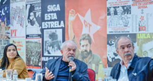 Foto de Lula em uma reunião com dirigentes do PT. Ao fundo, cartazes com fotos do ex-presidente.