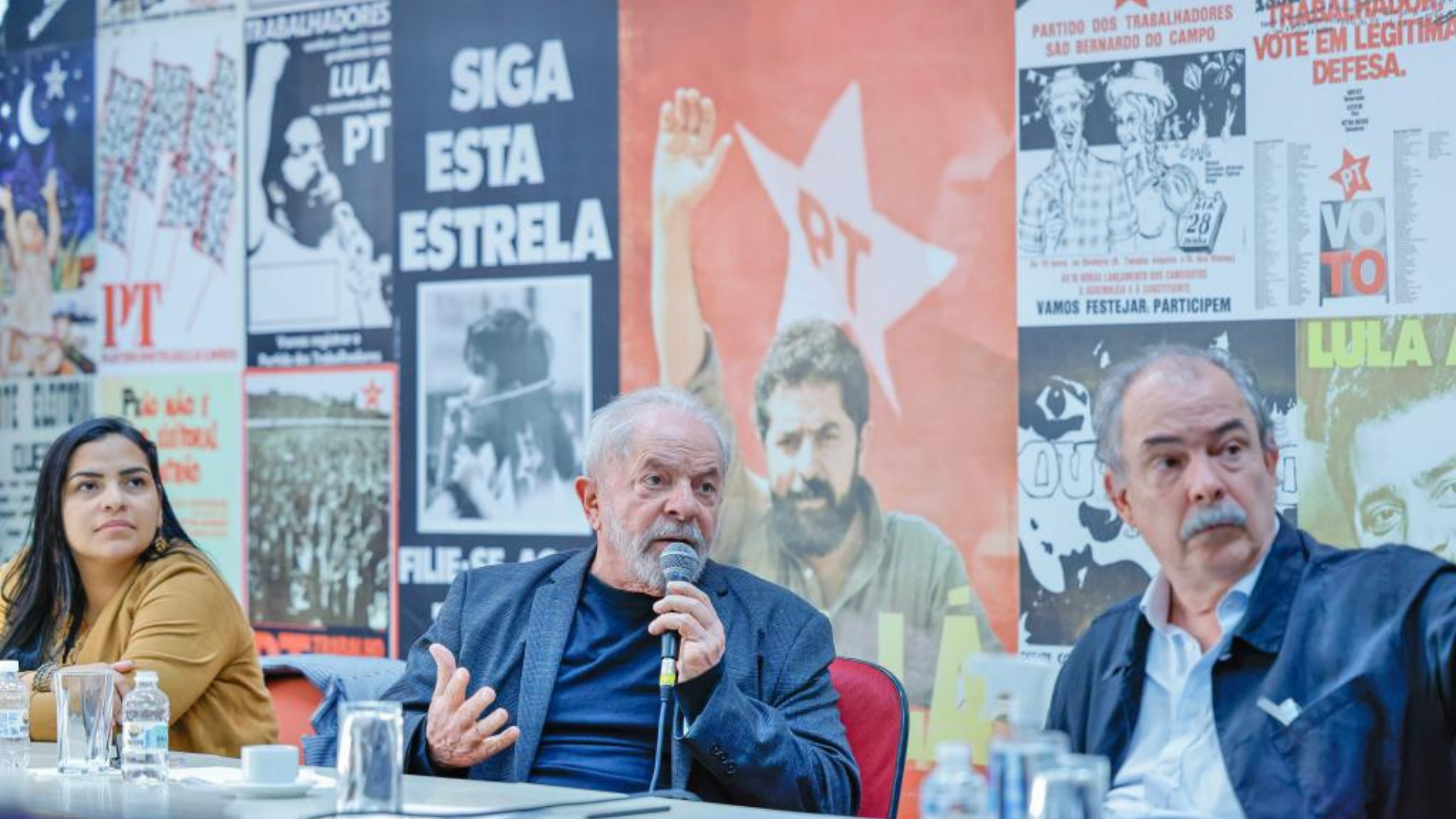 Foto de Lula em uma reunião com dirigentes do PT. Ao fundo, cartazes com fotos do ex-presidente.