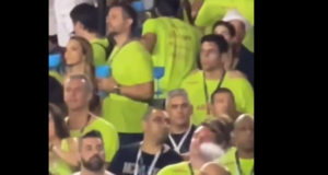 Foto de foliões em uma arquibancada. O senador Flávio Bolsonaro aparece com uma camisa verde fumando