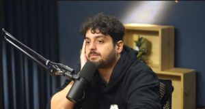 Foto de Monark com olhar sério e mão direita na bochecha.