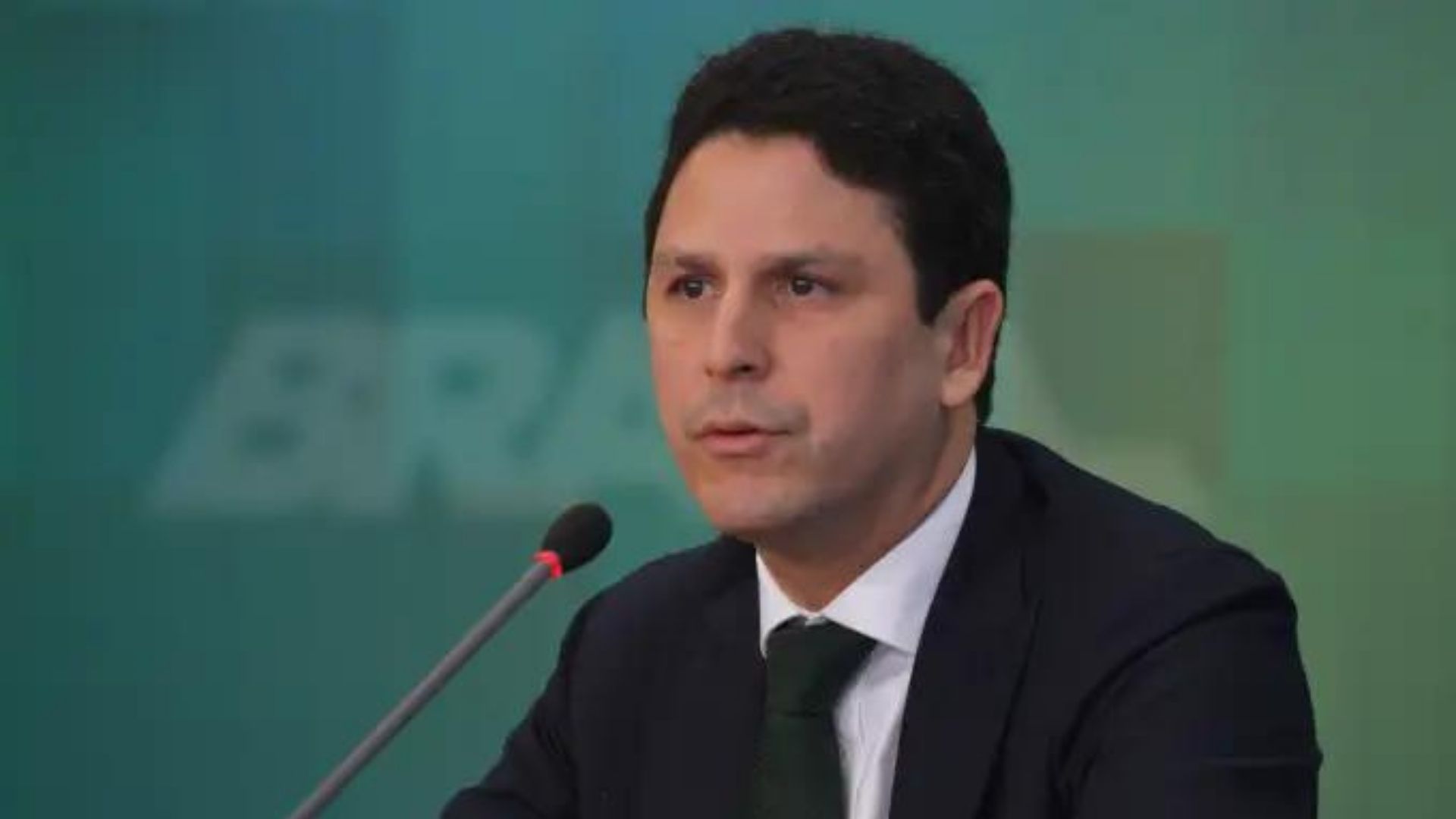 Foto de Bruno Araújo usando terno preto e falando ao microfone.