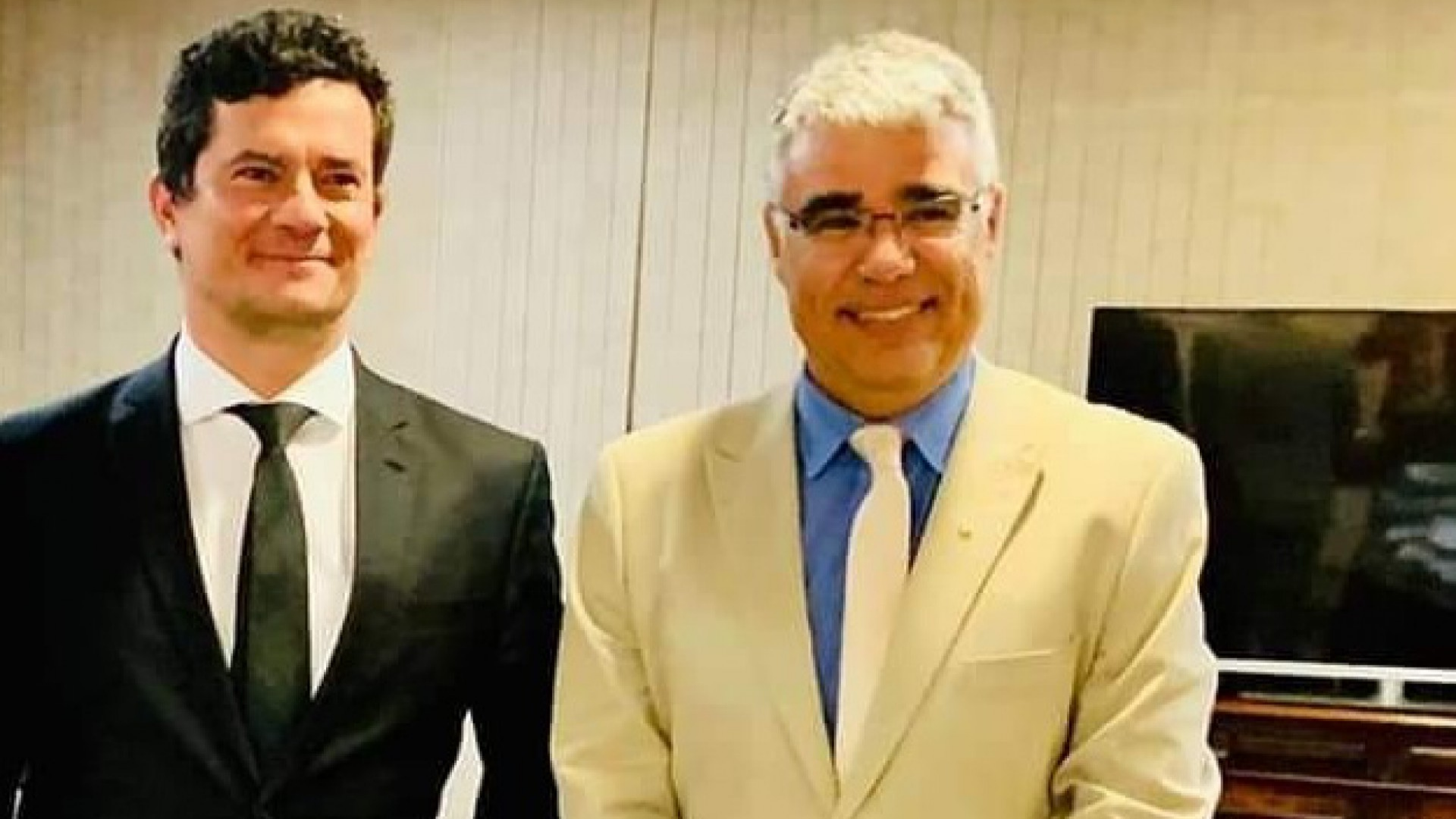 Senador Girão bancou viagem de Moro à Alemanha. Foto de Moro, com terno preto e sorrindo, ao lado de Girão, com terno branco, óculos de grau e sorrindo.