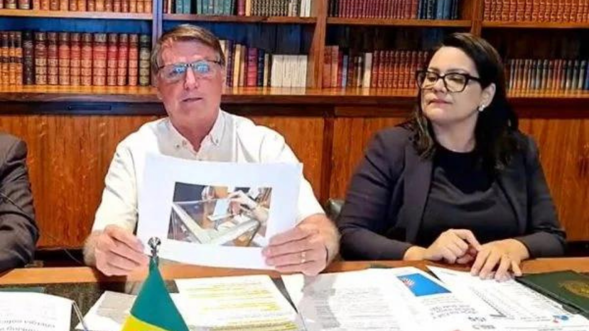 Foto de Bolsonaro segurando uma foto de uma urna durante a live semanal na quinta-feira (14).