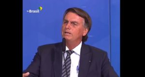 Foto de Bolsonaro com expressão desconcertada enquanto fala ao microfone.