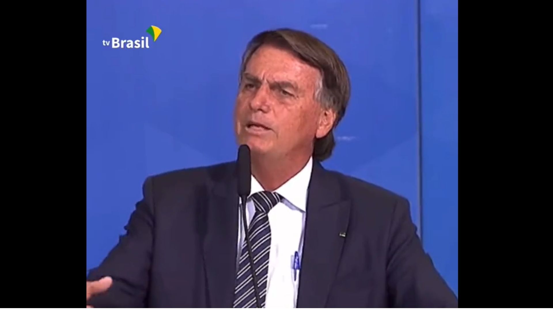 Foto de Bolsonaro com expressão desconcertada enquanto fala ao microfone.