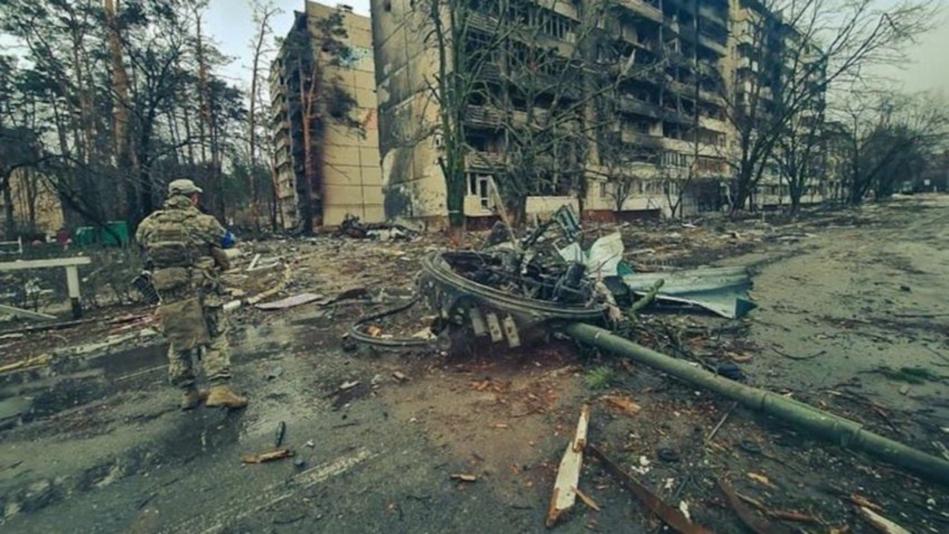 Foto de uma área na Ucrânia com um prédio destruído e um militar visualizando a situação.