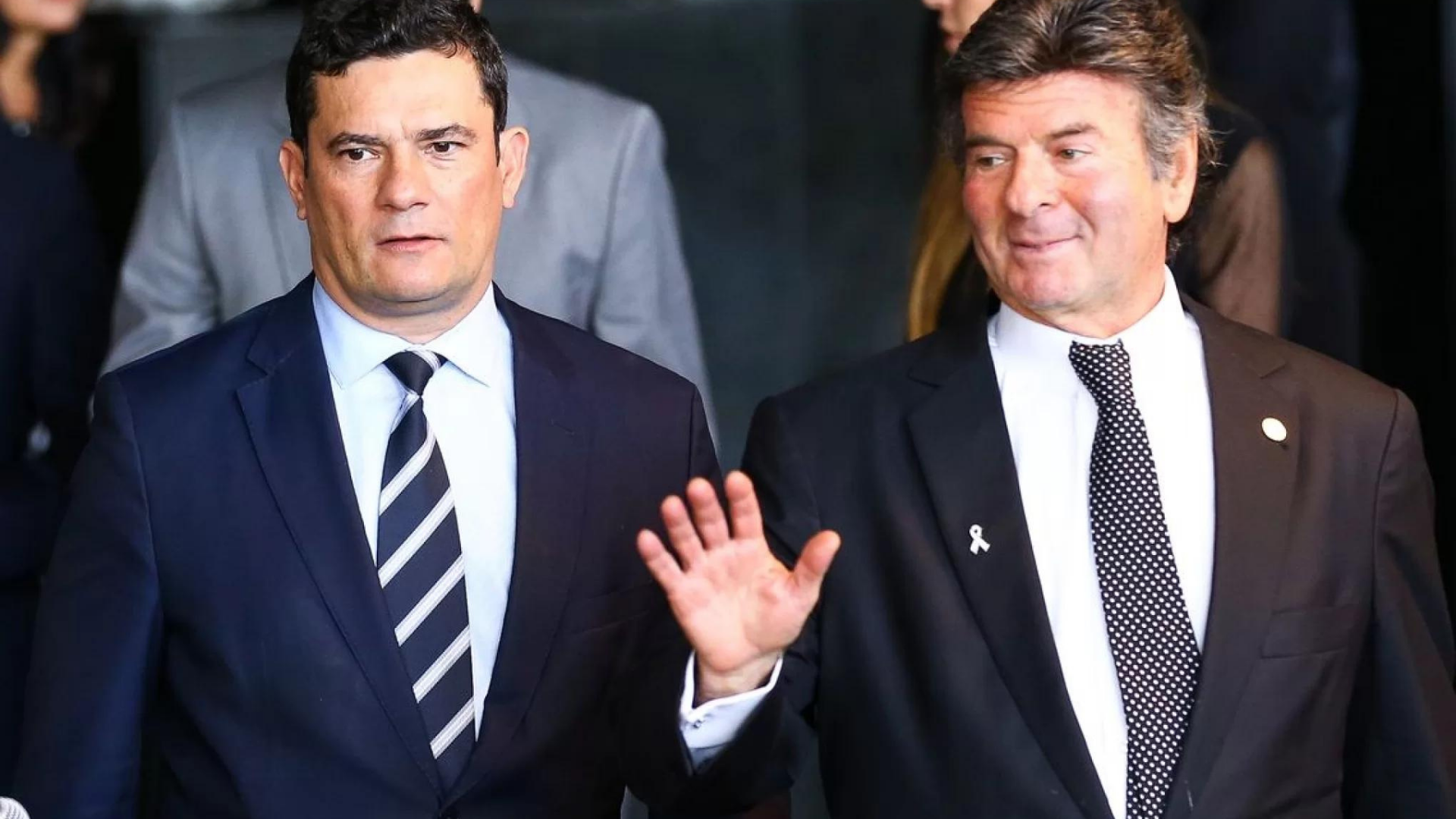 Foto de Sergio Moro ao lado de Luiz Fux, que está sorrindo e acena com a mãe direita.