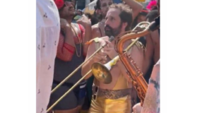 Gregorio Duvivier aparece com pele branca, barba e cabelos pretos, calça na cor dourada e sem camisa curtindo o carnaval do Rio.