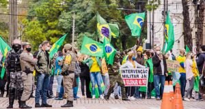 Foto de manifestantes bolsonaristas com camisas do Brasil, bandeiras do país e cartazes com frases conservadoras.