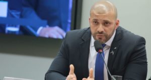 Foto de Daniel Silveira com olhar sério enquanto fala o microfone.
