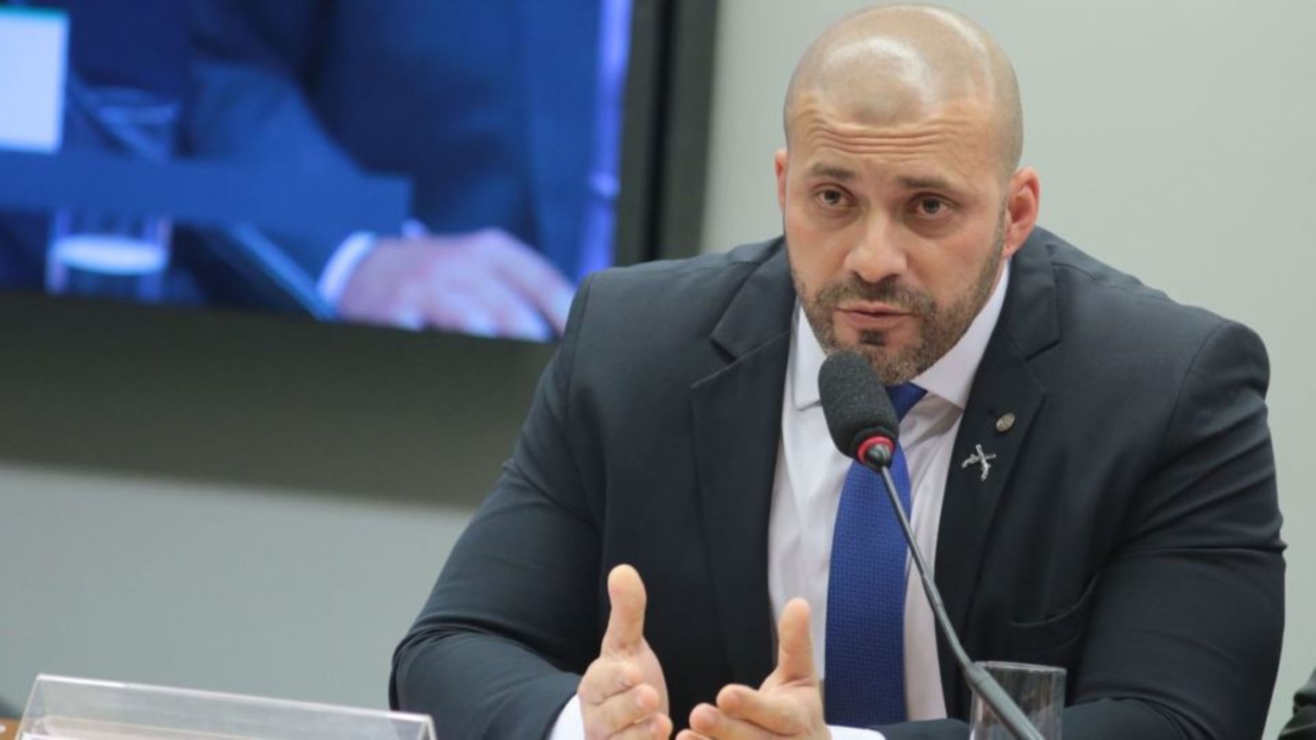 Foto de Daniel Silveira com olhar sério enquanto fala o microfone.