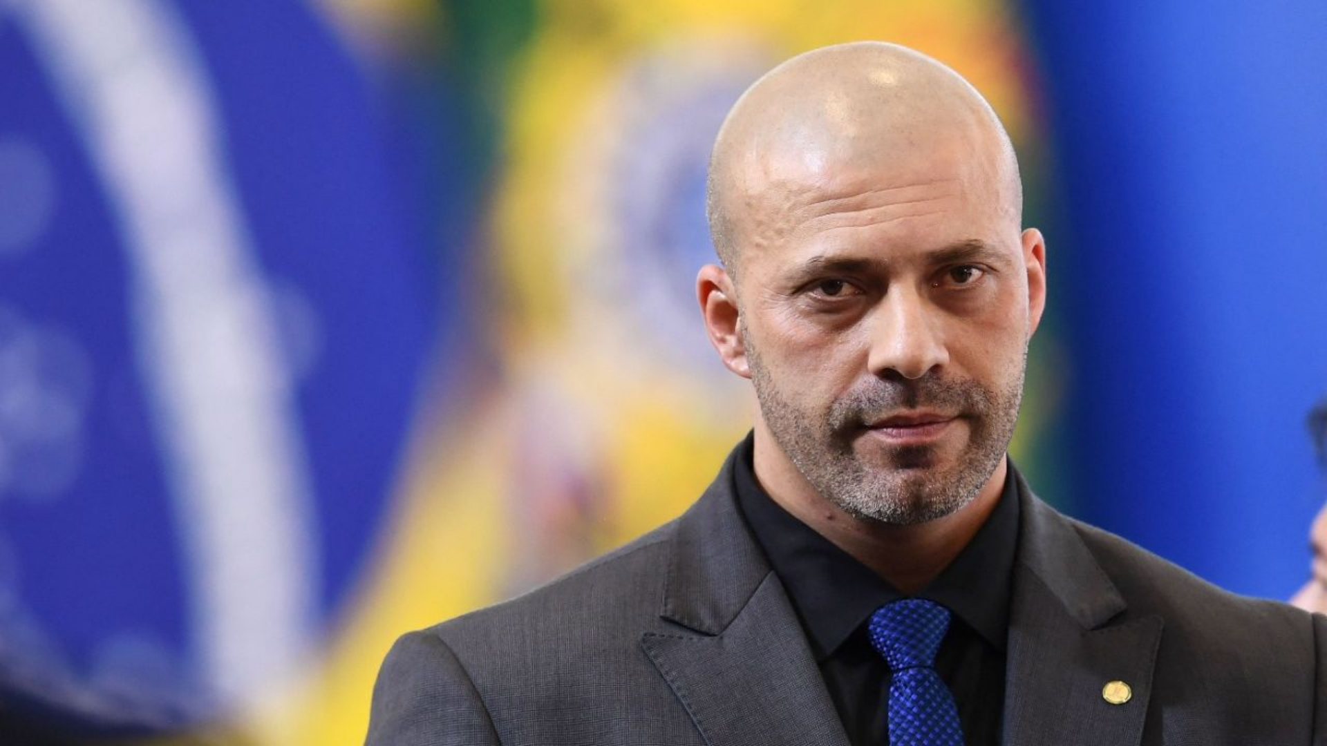 PF vai ter que tomar depoimento de Daniel Silveira em até 15 dias, ordena Moraes. Foto de Daniel Silveira com expressão séria, cabelo calvo e terno azul.