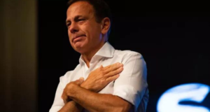 PT vai ao Ministério Público contra João Doria. Foto de João Doria com camisa branca e abraçando a si mesmo.