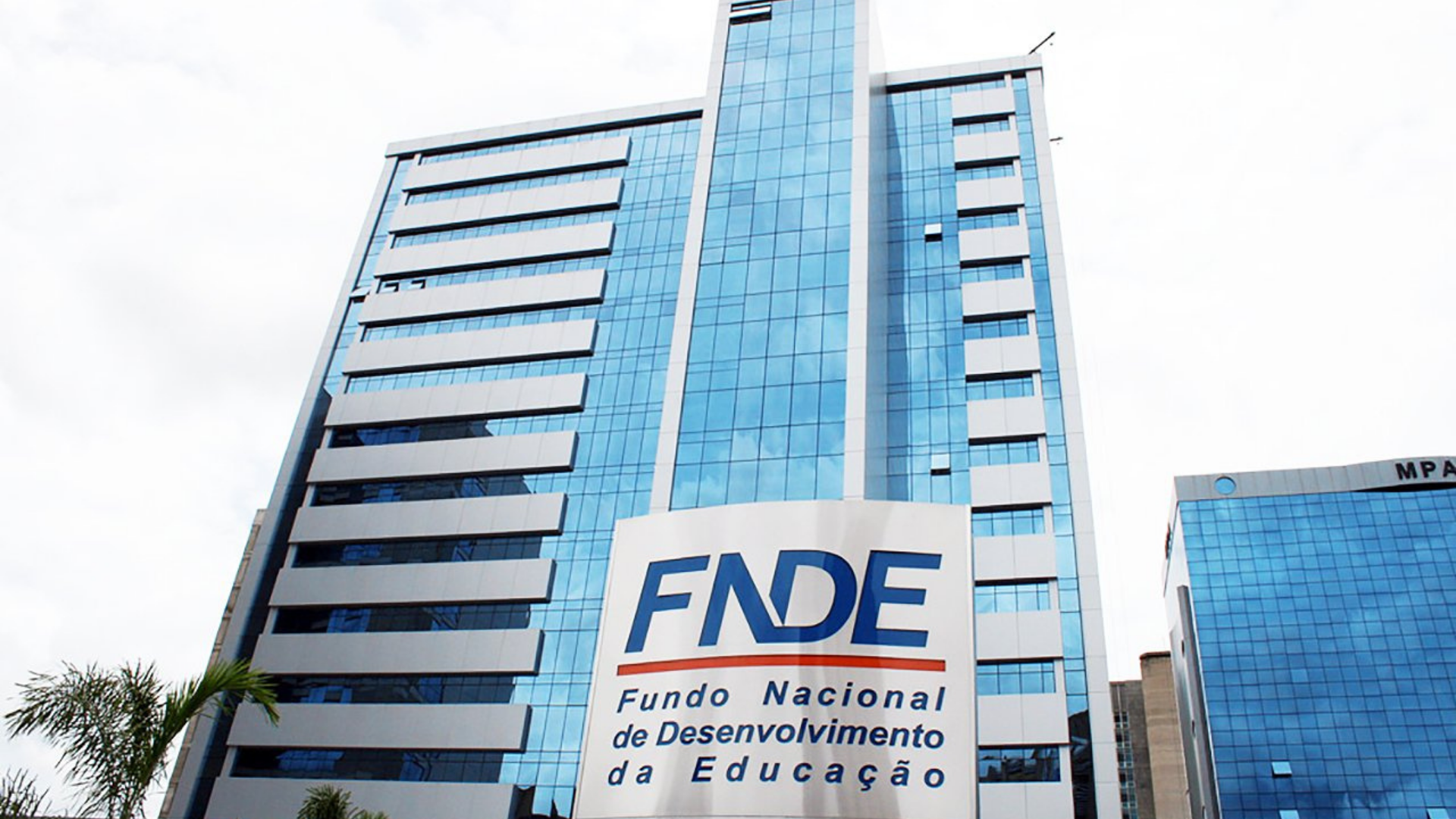 Foto da fcahada do FNDE, prédio de vários andares com janelas de vidro.