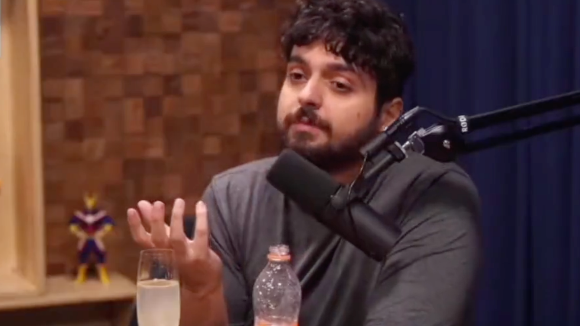 Monark chama Kim Kataguiri na semana de estreia de seu novo podcast. Foto de Monark, com barba e cabelos pretos, sentado em uma cadeira falando ao microfone.