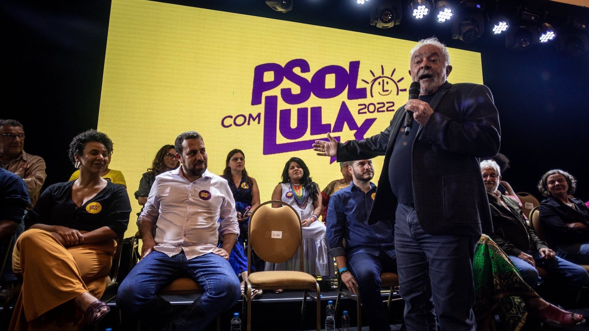 Foto do ex-presidente Lula falando em um palanque com o símbolo do PSOL ao fundo.