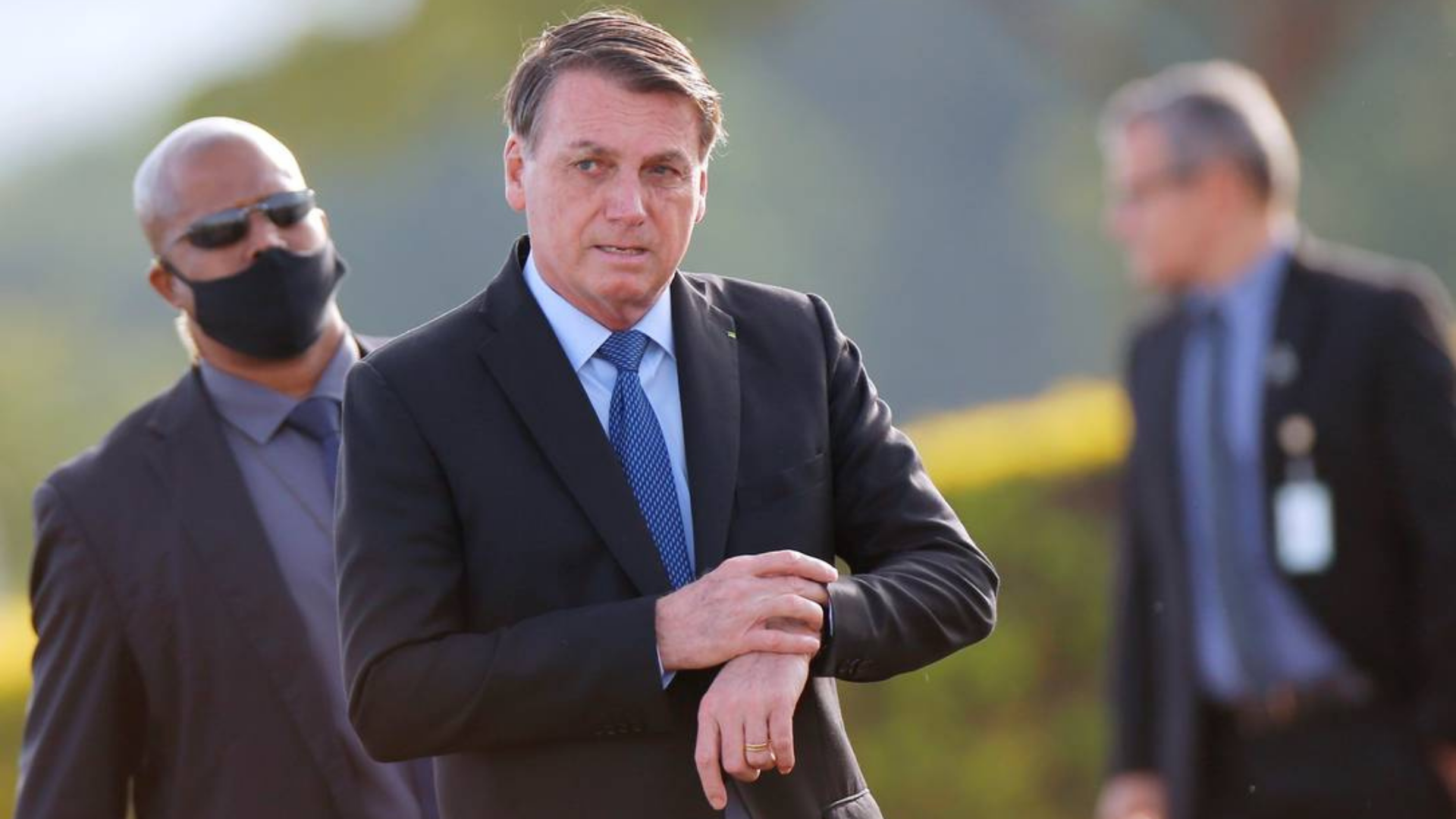 Bolsonaro usa terno preto e camisa branca e tem expressão desconcertada enquanto caminha.