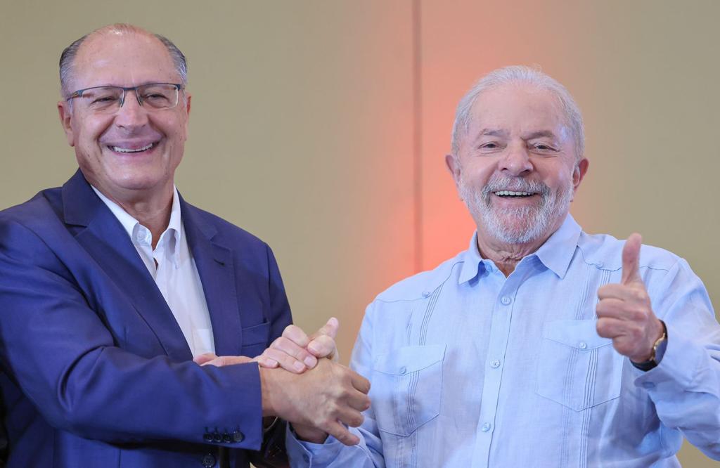 Alckmin e Lula felizes, apertando a mão e fazendo joinha.
