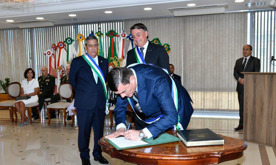 O novo ministro da Defesa, general Paulo Sérgio Nogueira, assinando o termo de posse em cerimônia. Bolsonaro e Braga Netto acompanham o momento, assim como outras autoridades.