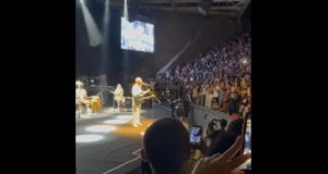 Na imagem, Gilberto Gil aparece no palco, enquanto a plateia canta a favor de Lula. Muitas pessoas aparecem com celulares para registrar o momento.