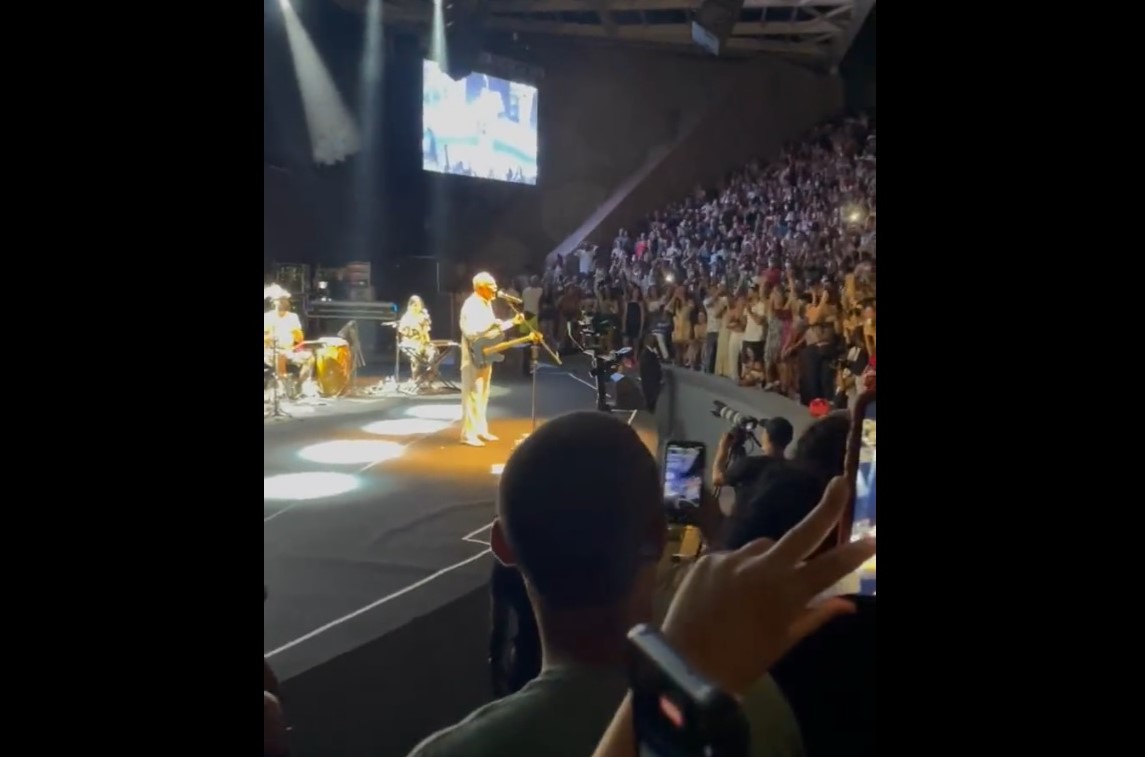 Na imagem, Gilberto Gil aparece no palco, enquanto a plateia canta a favor de Lula. Muitas pessoas aparecem com celulares para registrar o momento.