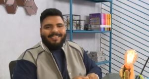O humorista Paulo Vieira, sentado e sorrindo, durante seu quadro no BBB.