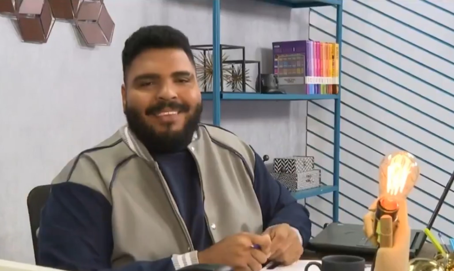 O humorista Paulo Vieira, sentado e sorrindo, durante seu quadro no BBB.