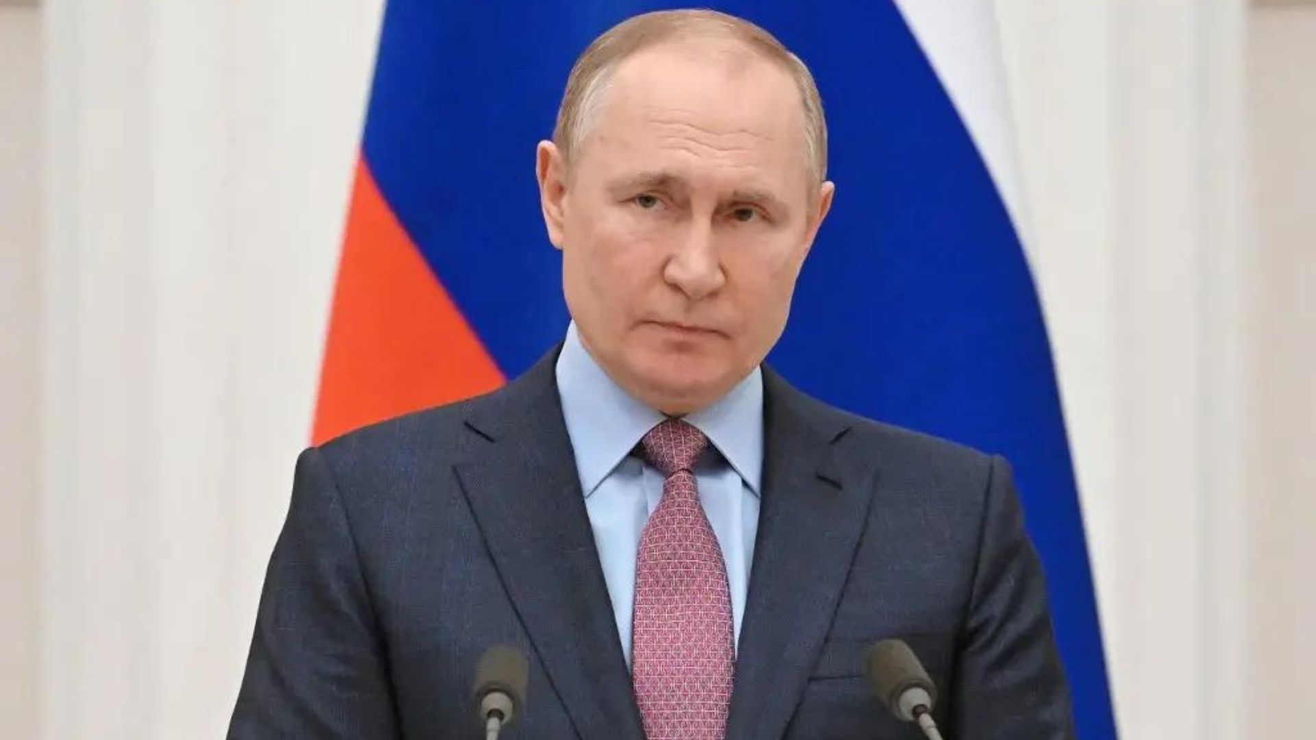 Foto de Putin com olhar sério para a câmera. Ao fundo, bandeira da Rússia.