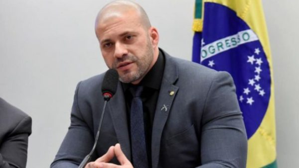 Daniel Silveira está sentado em local com terno cinza e cabeça careca.