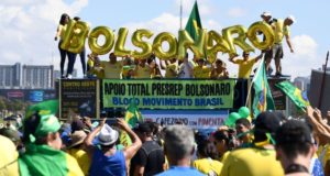 Foto de apoiadores do presidente Bolsonaro. Em um trio, diversos bolsonaristas seguram letras douradas que juntas formam o nome Bolsonaro.