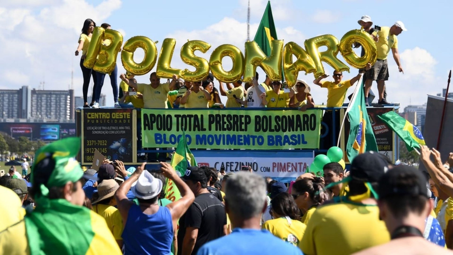 Foto de apoiadores do presidente Bolsonaro. Em um trio, diversos bolsonaristas seguram letras douradas que juntas formam o nome Bolsonaro.